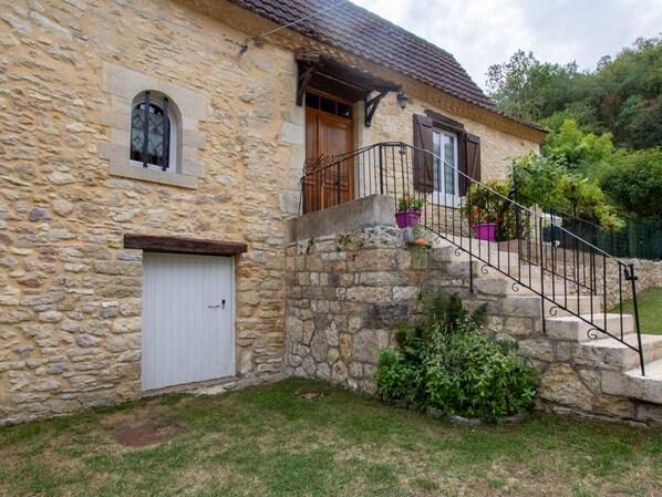 A stone house with a white door, a small window, and a staircase leading to a wooden balcony.