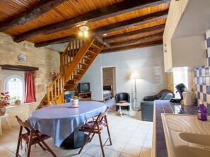 A rustic kitchen with a wooden staircase, a dining area with a round table, and a stone wall.