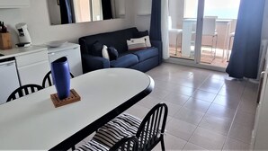 A compact living space with a kitchenette, a dining area with a table and chairs, a sofa, and a sliding glass door leading to an outdoor area. - T2 Apartment in Banyuls, terrace, parking, WIFI (Banyuls-sur-Mer)