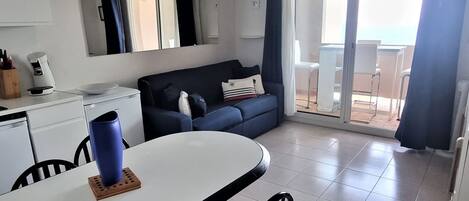 A compact living space with a kitchenette, a dining area with a table and chairs, a sofa, and a sliding glass door leading to an outdoor area.