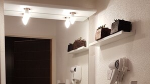 Un baño con un lavamanos blanco, un espejo, un secador de pelo y un perchero para toallas.