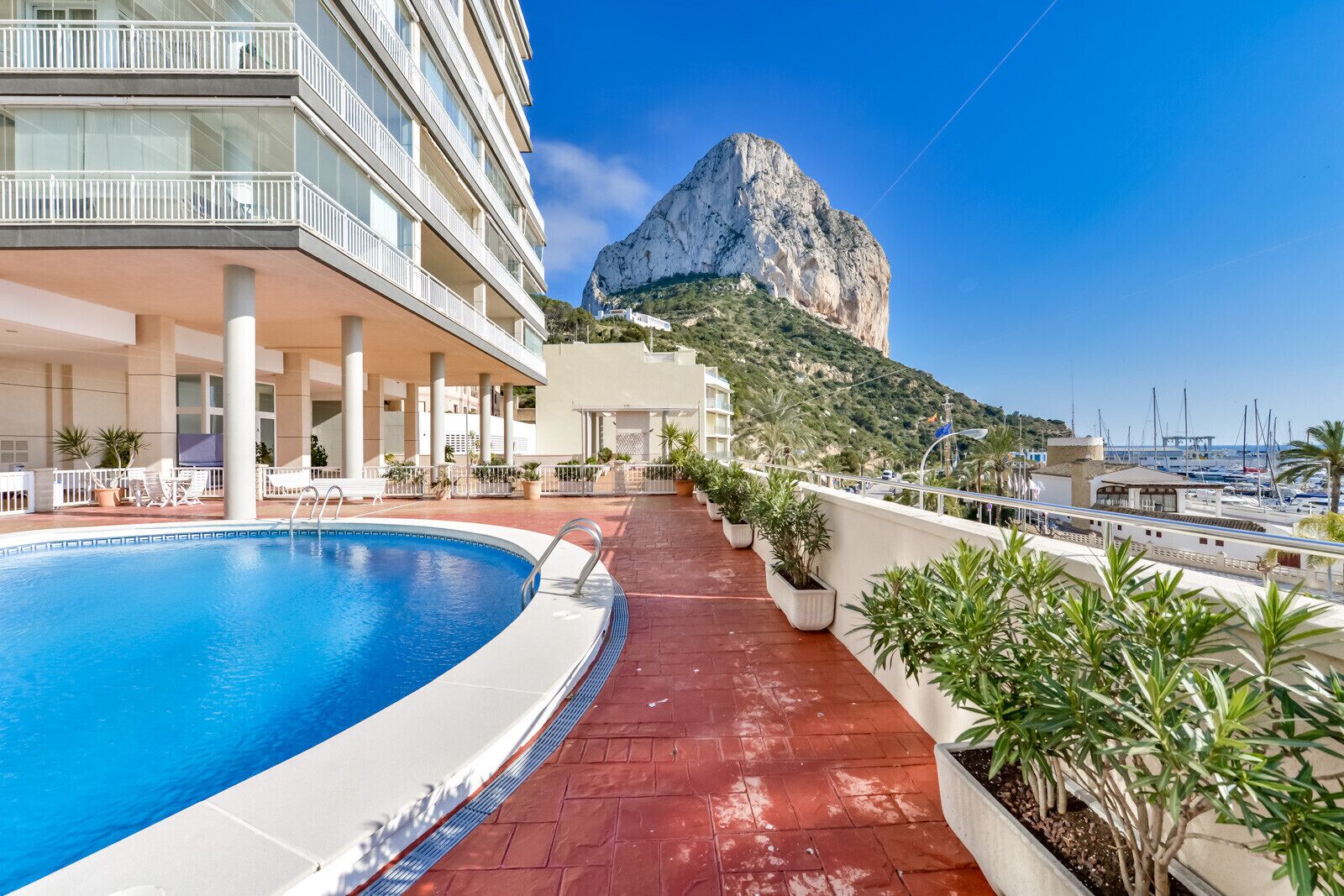 A hotel pool area with a clear view of a mountain and marina in the background.