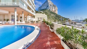 A hotel pool area with a clear view of a mountain and marina in the background.