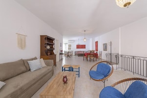 Una sala de estar con sofá, mesa de centro y sillas, un comedor con mesa y sillas, y una escalera con barandilla.