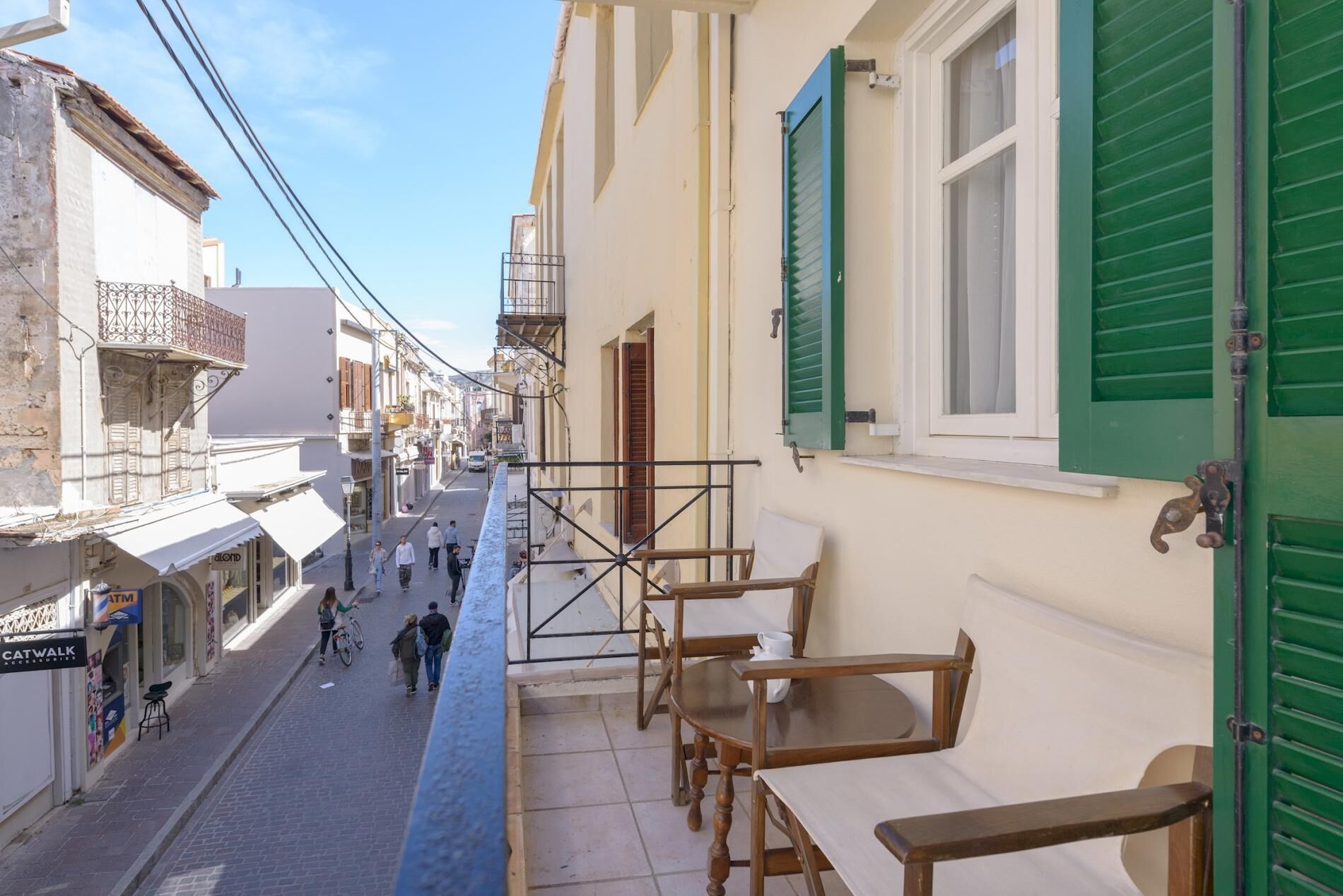 Una calle estrecha flanqueada por edificios, con mesas al aire libre y algunos peatones.