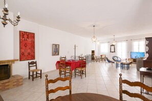 Ein geräumiges Wohnzimmer mit Kamin, einem Essbereich mit rotem Tischlein und einem Fernseher.