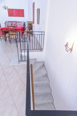 A staircase with a handrail, a dining area with a red tablecloth, and a wall with a decorative light fixture.