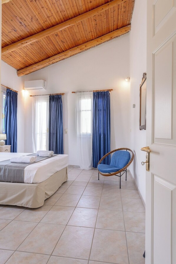 A bedroom with a wooden ceiling, a bed, a chair, and curtains.