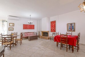 A dining area with a red tablecloth, wooden chairs, a sofa, and a fireplace.