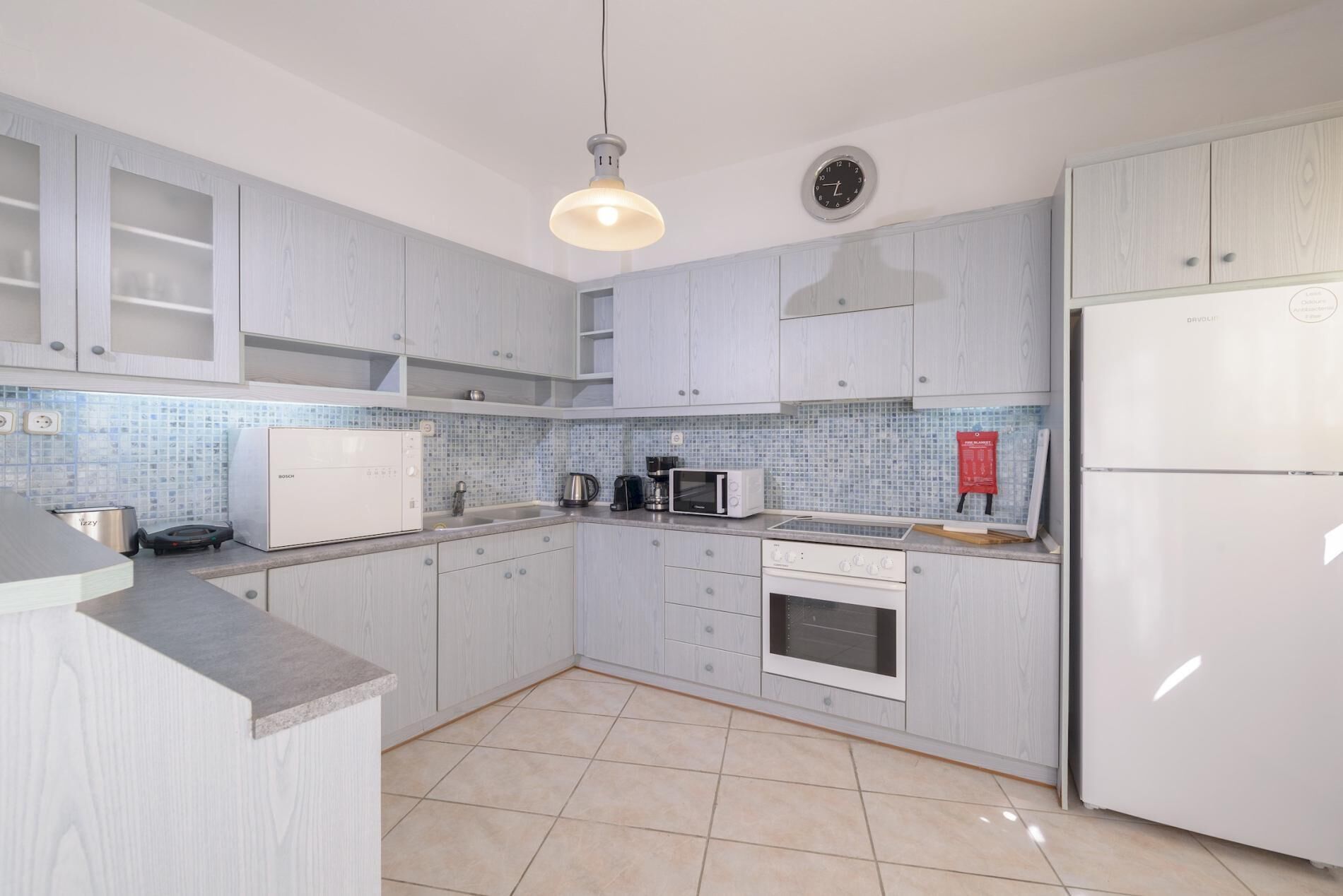 A modern kitchen with light wood cabinetry, a Bosch microwave, a coffee maker, and a refrigerator.