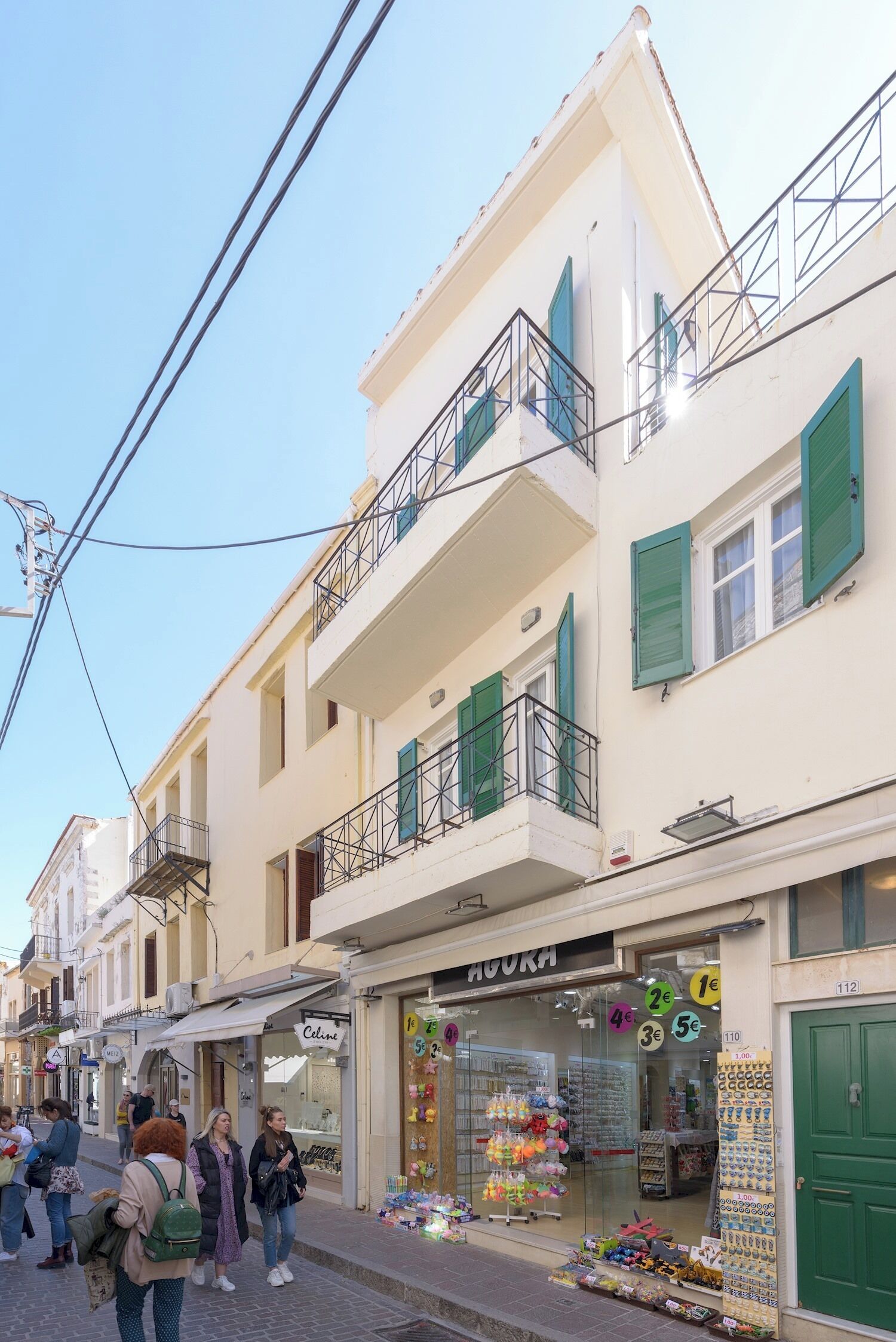 Uma rua com edifícios altos, uma vitrine visível com um letreiro e pedestres.