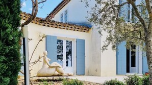 A stone wall, a wooden table with a bottle and glasses, and a house with blue shutters and a tiled roof. - Villa de Charme, à Proximité Immédiate D'uzes et du Pont du Gard (Argilliers)