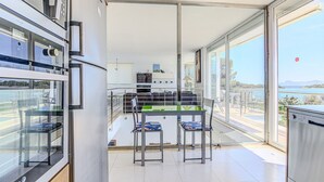 Eine moderne Küche mit Essbereich aus Glas, Edelstahlgeräten und Blick aufs Meer.