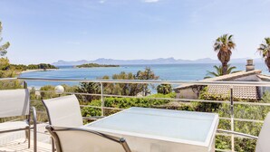 Ein Balkon mit Tisch und Stühlen mit Blick auf die Küste und Berge in der Ferne.