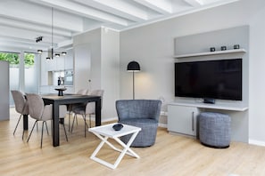 Una sala de estar moderna con comedor, un sillón tapizado gris, una mesa de centro blanca y un televisor de pantalla plana montado en la pared.