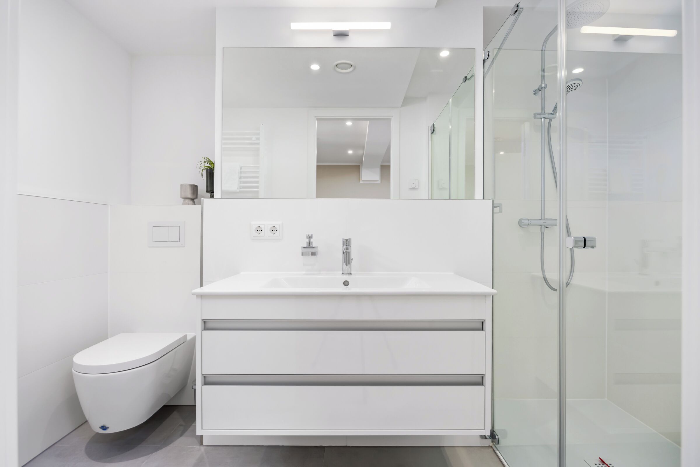 Un baño moderno con tocador blanco, inodoro y cabina de ducha de vidrio.