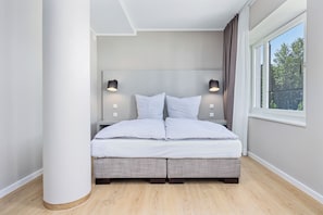 Quarto moderno com uma cama grande, duas luminárias de cabeceira e uma janela com vista para árvores.