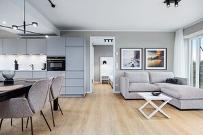 Une cuisine moderne dotée d’appareils électroménagers intégrés, un coin repas avec une table et des chaises, un canapé gris et une petite table blanche.