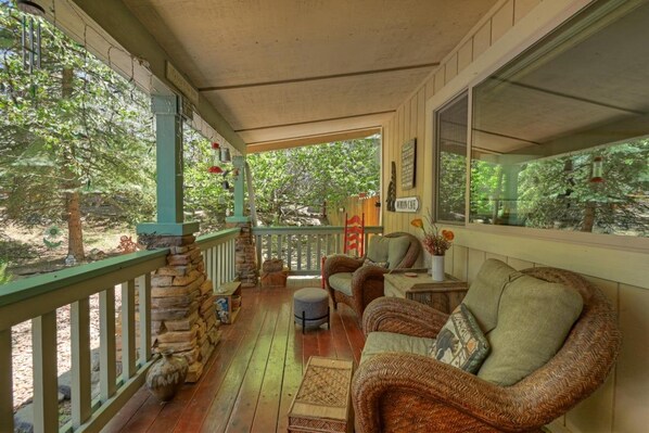 A covered porch with wicker furniture, a stone wall, and a view of the surrounding trees.