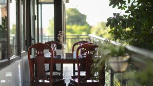 A dining area with a table set for two, wooden chairs, and a view of greenery outside. - Nam Hai Hotel (Hanoi)