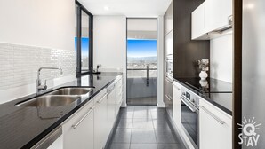 A modern kitchen with a large window, stainless steel appliances, and a view of the city. - The Wave - 3 Bedroom Broadbeach Apartment (Broadbeach)