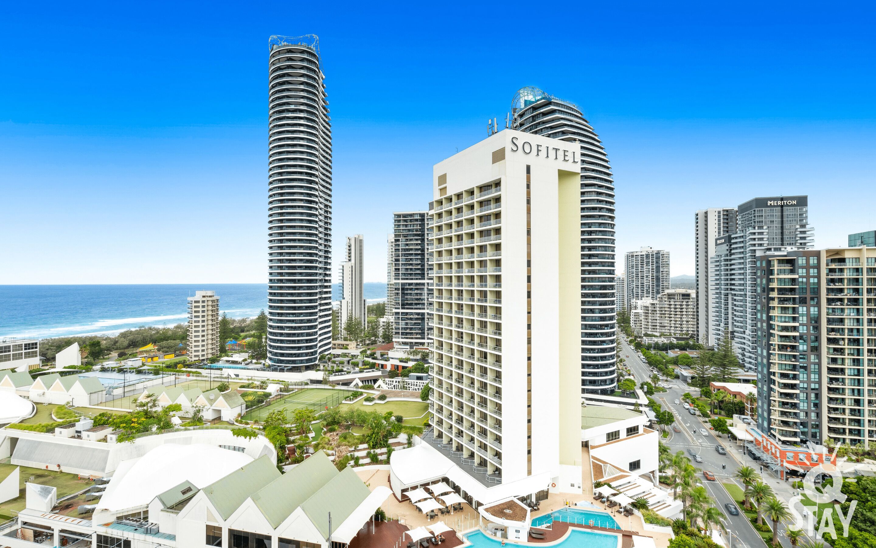 Een hoog hotel met zwembad, omringd door andere hoge gebouwen en uitzicht op de oceaan.