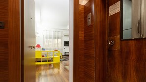 Eine Holztür, die in einen Raum führt, mit einem gelben Sofa, einem kleinen Tisch und einem mit Vorhängen drapierten Fenster.