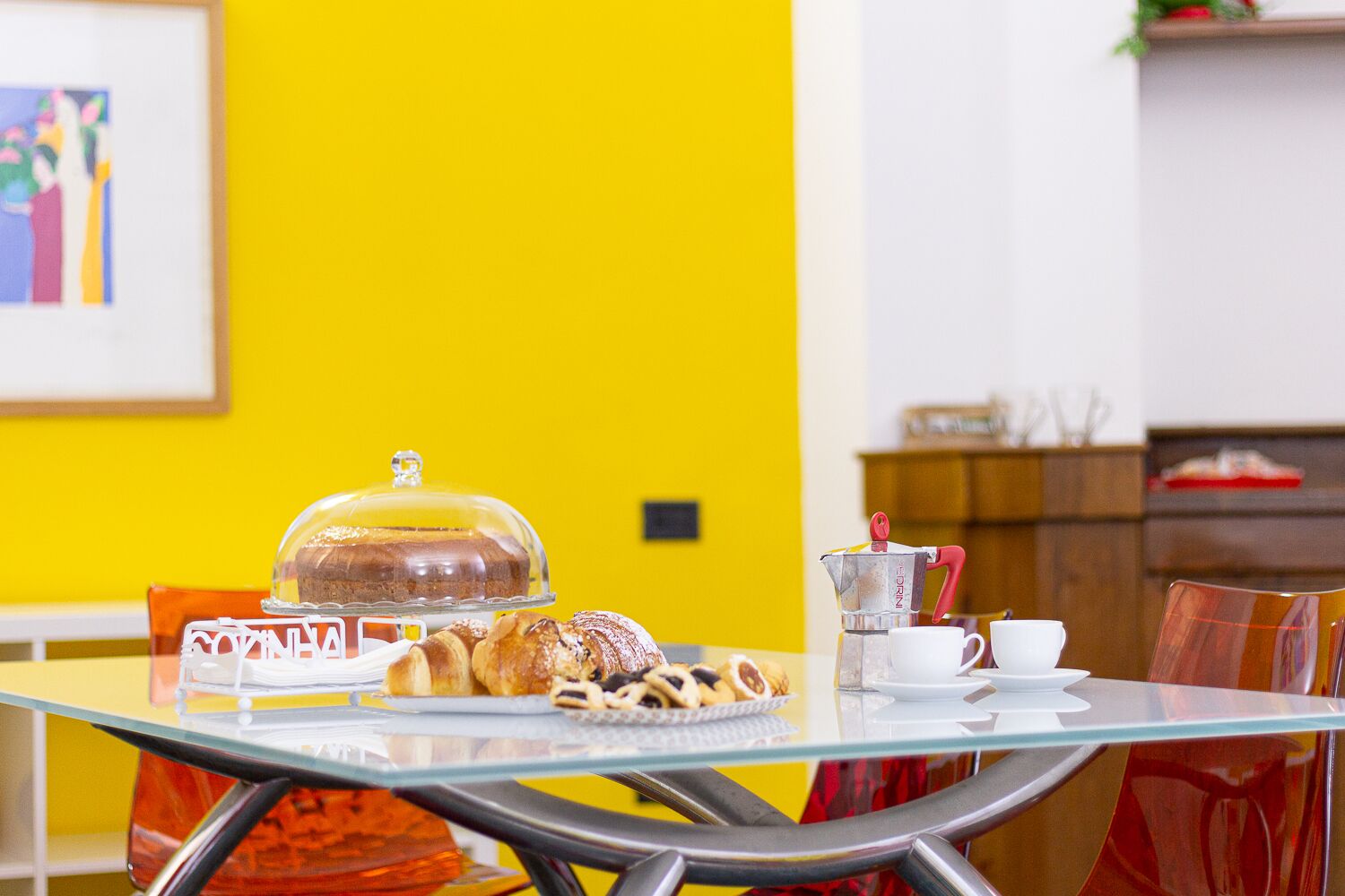 A breakfast table with pastries, a coffee pot, and a glass display case with a loaf of bread.