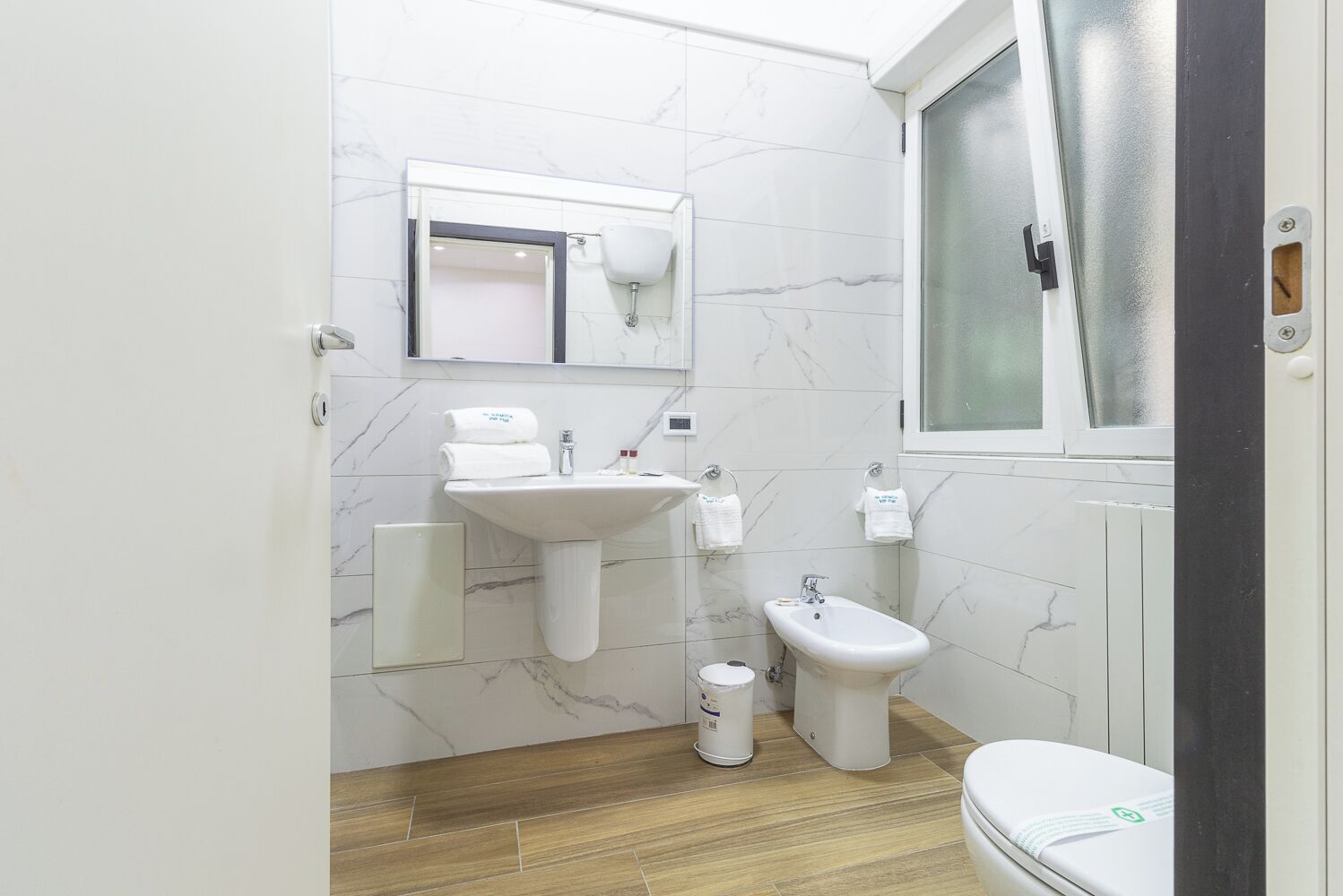 Un baño pequeño con lavamanos pedestal, un bidé, un inodoro y una ventana.
