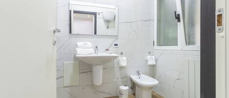 Un baño pequeño con lavamanos pedestal, un bidé, un inodoro y una ventana.