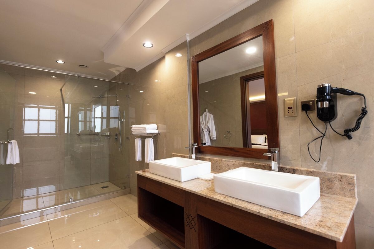 Un baño moderno con dos lavamanos, una cabina de ducha con mampara de vidrio y un secador de pelo en la pared.