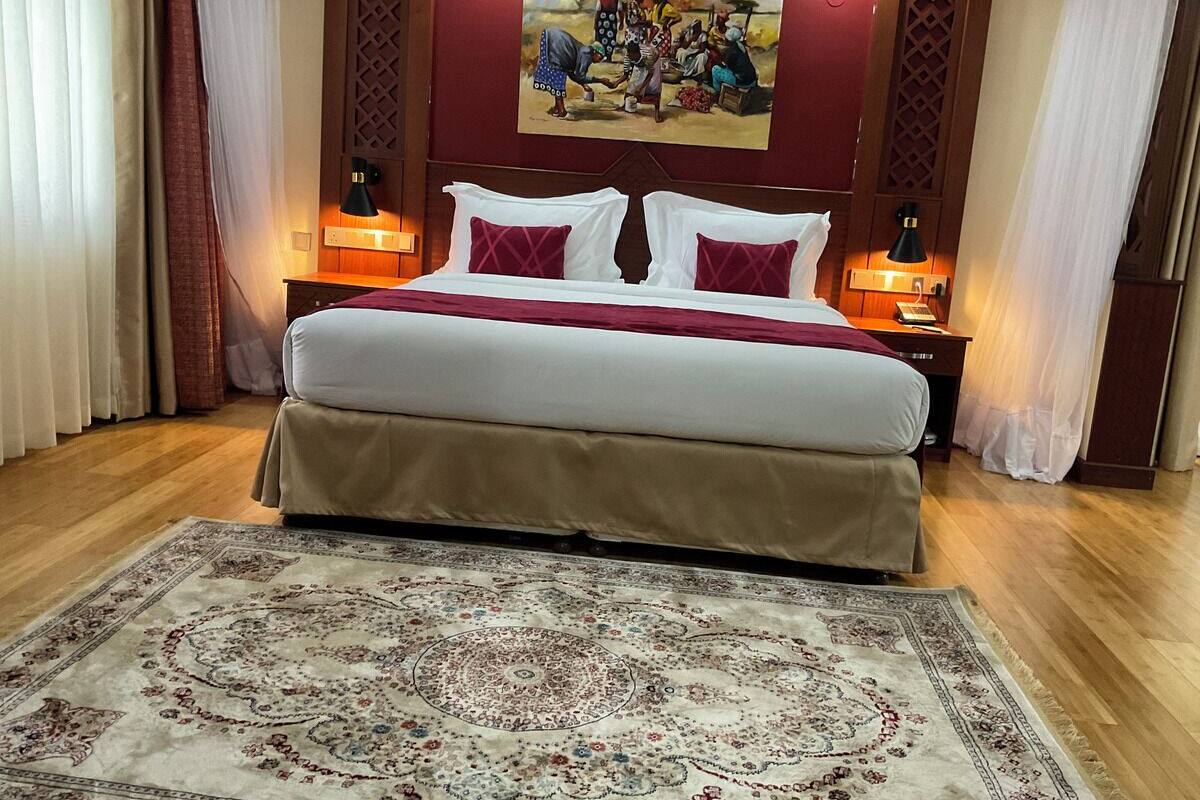 Une chambre d’hôtel avec un grand lit, deux tables de chevet avec des lampes, un tableau au mur et un tapis à motifs.