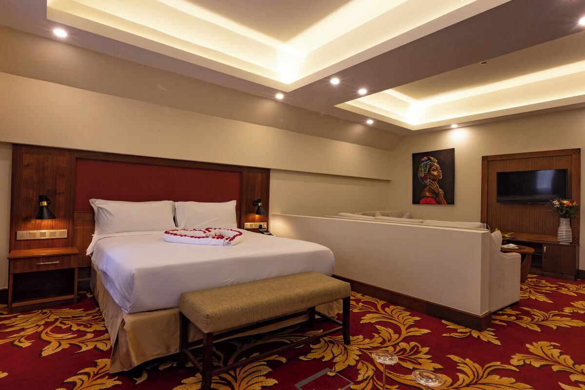 Ein Hotelzimmer mit einem großen Bett, einer Bank, einem Schreibtisch, einem Fernseher und einem Gemälde an der Wand.