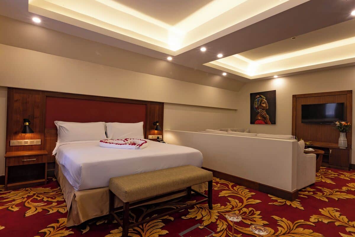 Une chambre d’hôtel avec un grand lit, une banquette, un bureau, une télévision et un tableau au mur.