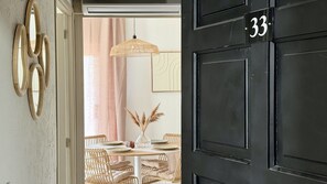 A black door with the number 33, a dining area with wicker chairs and a table, and a hanging light fixture.