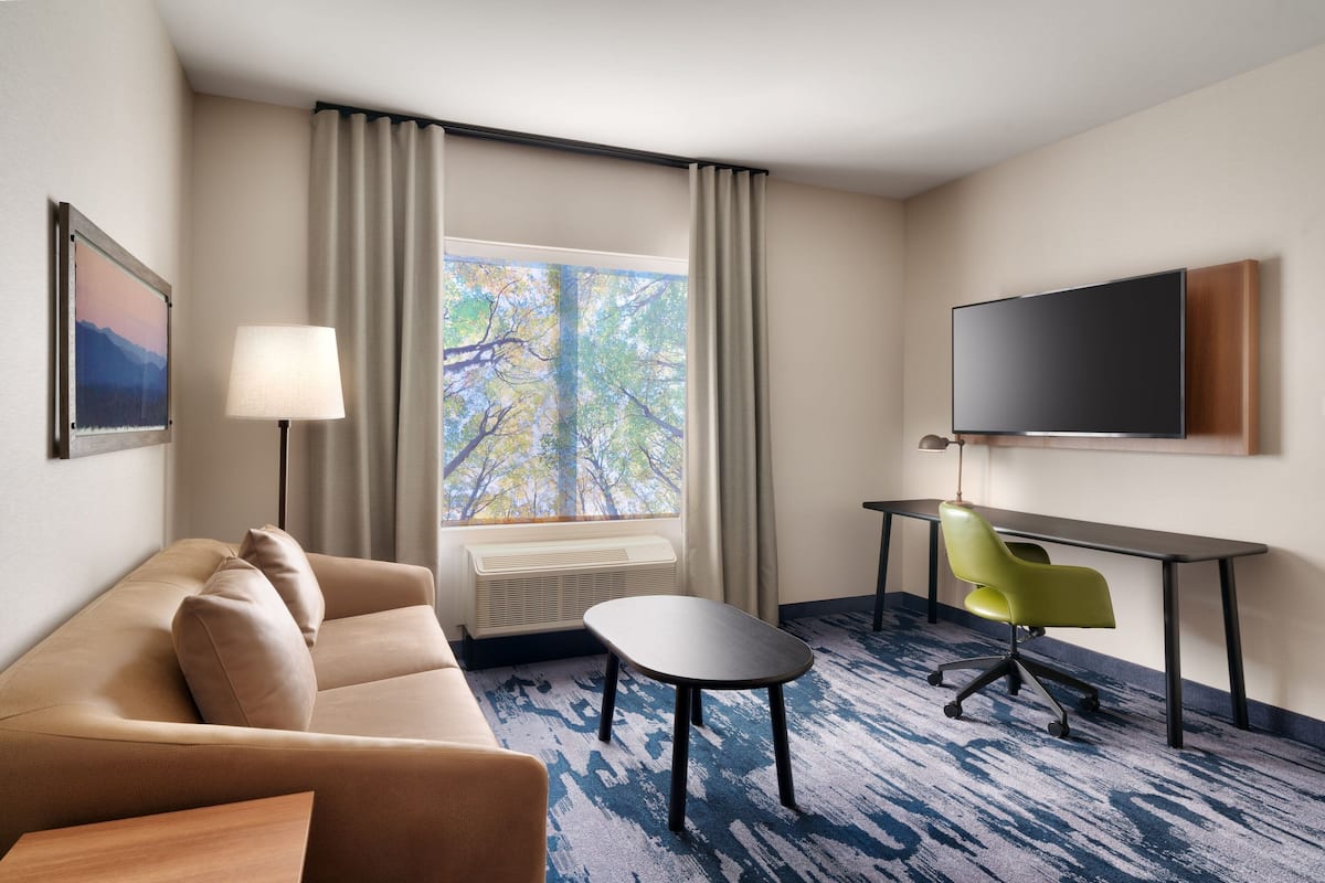 Une chambre d’hôtel avec un canapé, une petite table, une télévision et une fenêtre avec des rideaux.