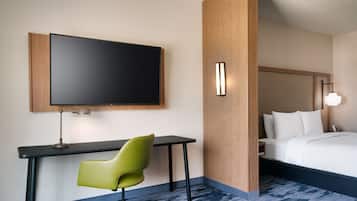 A hotel room with a bed, a desk with a chair, a flat-screen TV, and a wall-mounted light fixture.