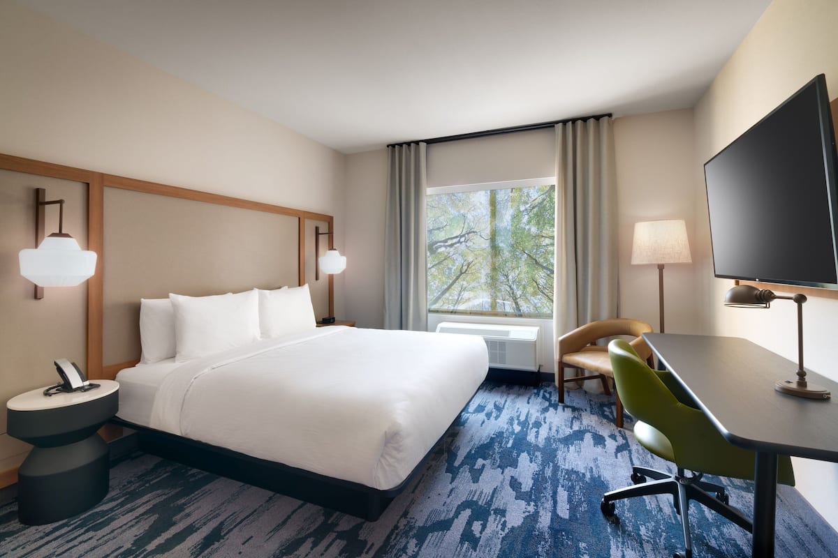 Une chambre d’hôtel avec un grand lit, un bureau, une chaise, une télévision et une fenêtre avec des rideaux.