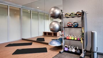A modern gym with exercise equipment, including a weight rack, kettlebells, and exercise balls.