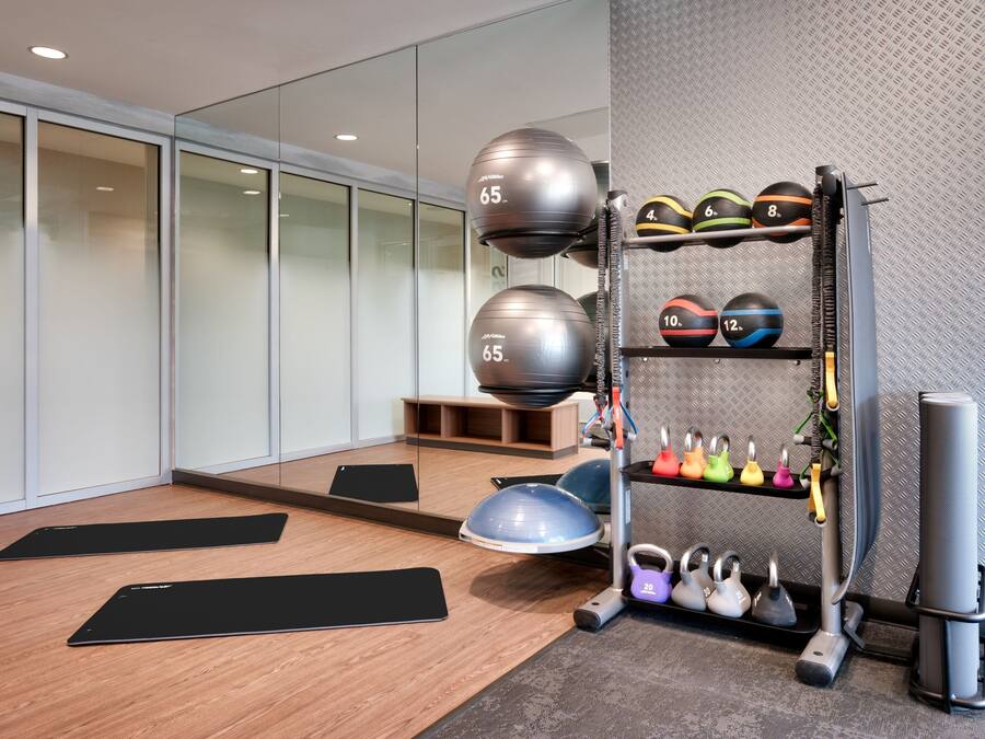 A modern gym with exercise equipment, including a weight rack, kettlebells, and exercise balls.