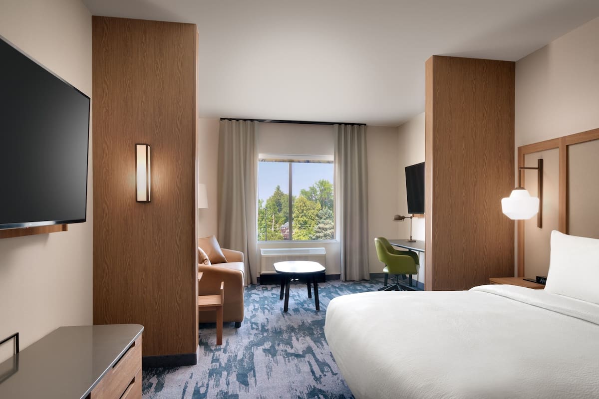 Une chambre d’hôtel avec un grand lit, un bureau, une chaise, une télévision et une fenêtre avec des rideaux.