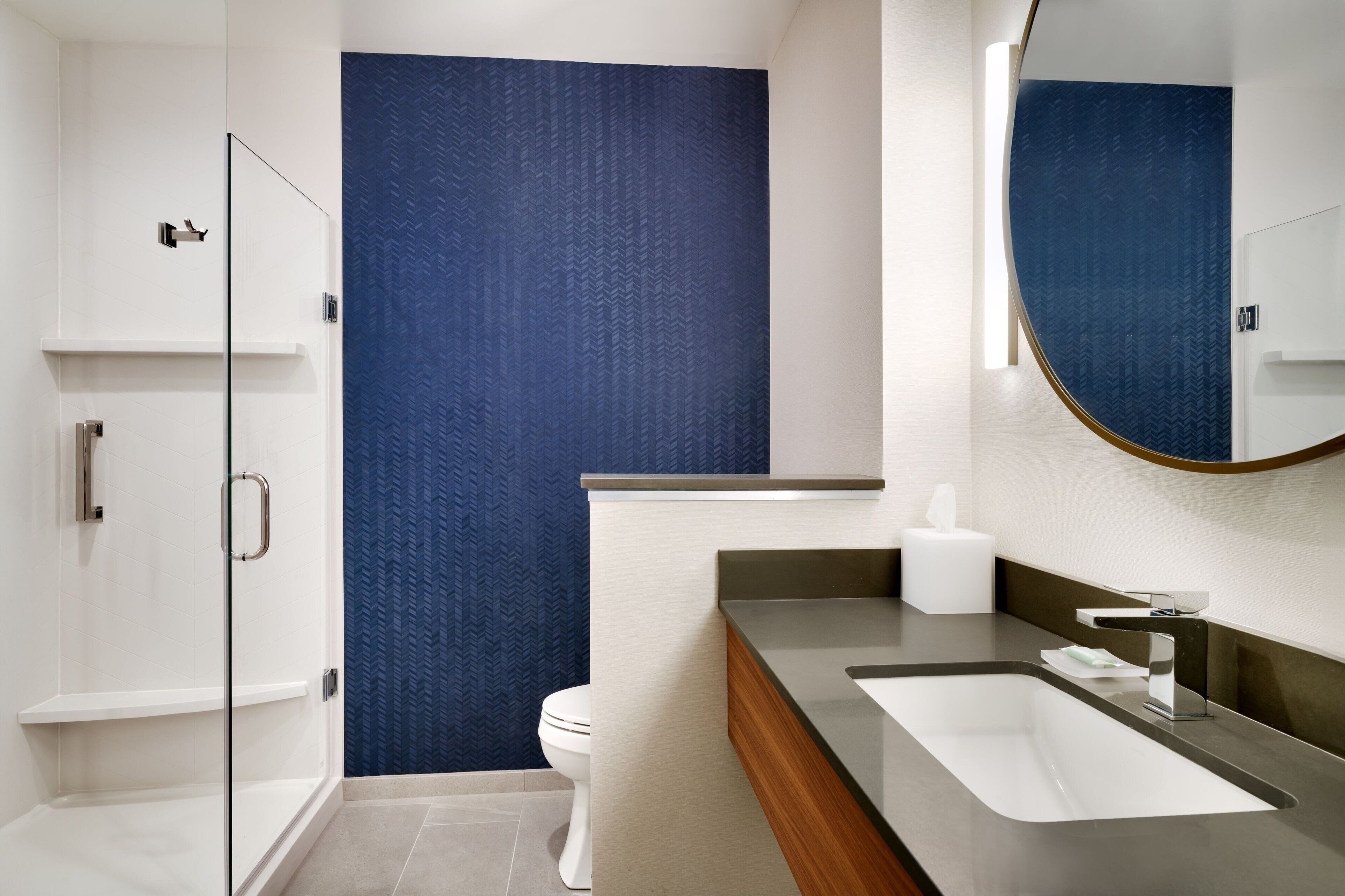Une salle de bain moderne avec une douche à parois de verre, des toilettes blanches et un meuble-lavabo avec un évier et un miroir.