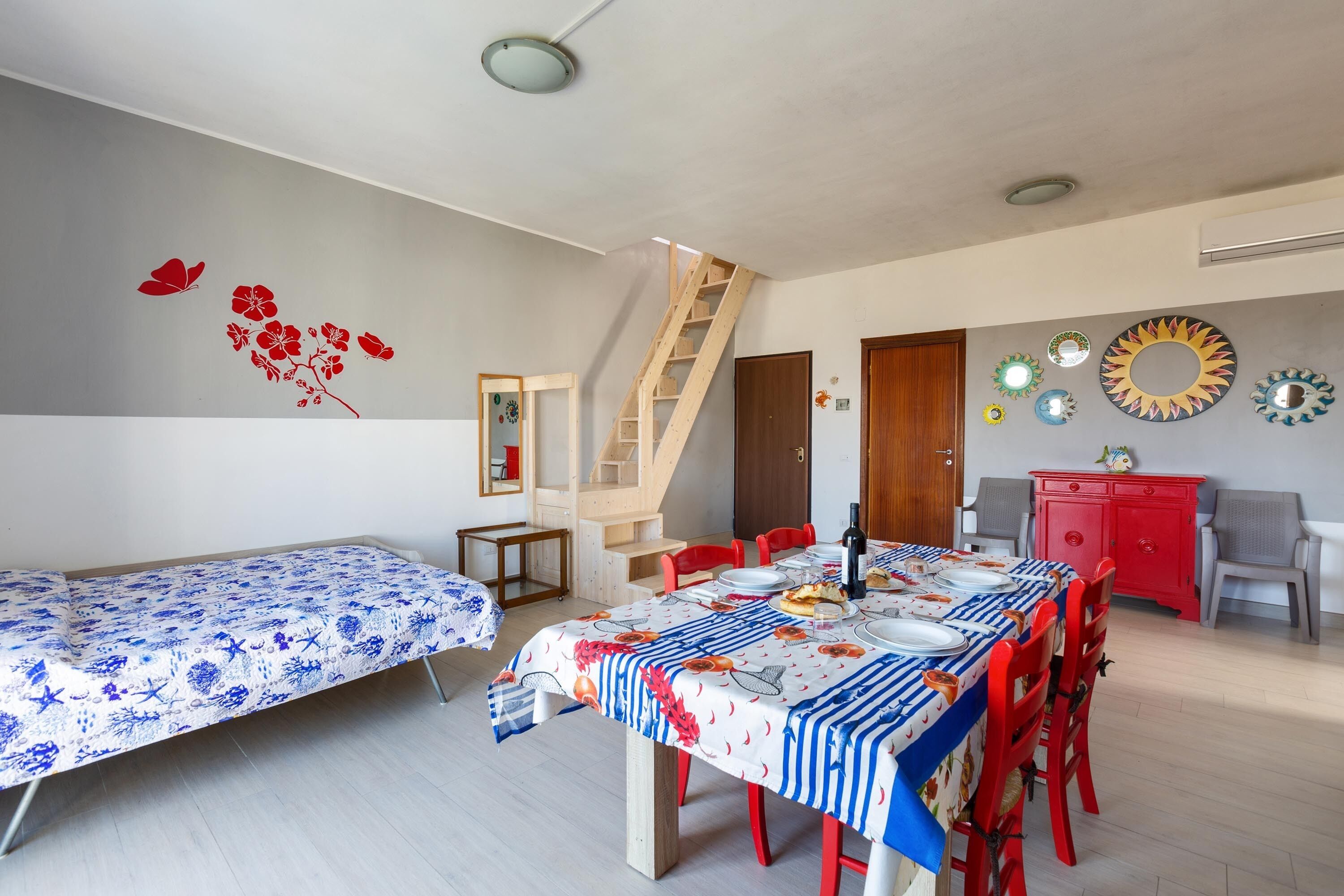 Une pièce comprenant une table à manger dressée pour quatre personnes, un escalier et un buffet rouge.