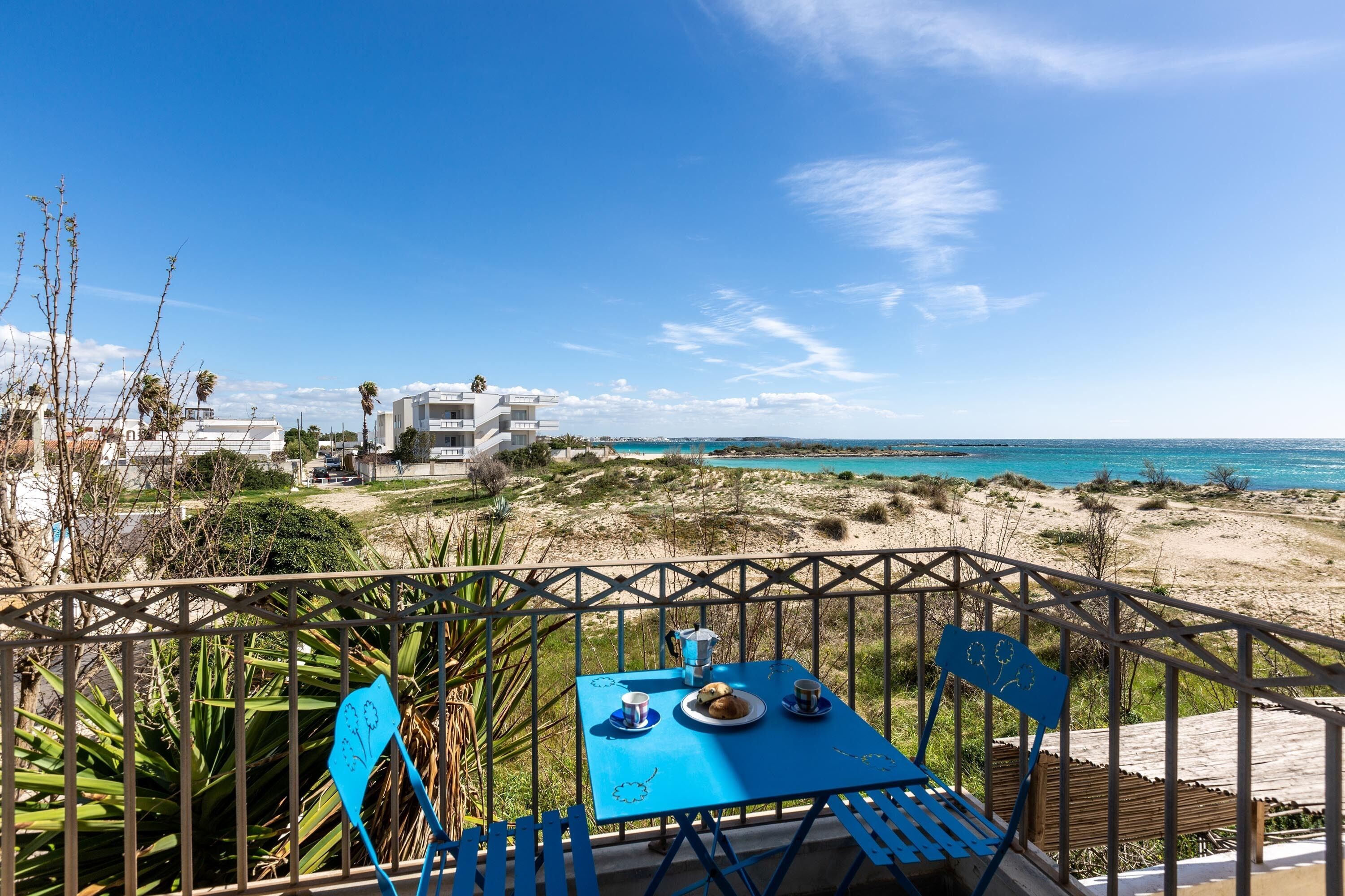 A blue table with two chairs on a balcony overlooking a beach and a building.