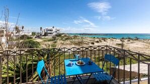 Una mesa azul con dos sillas en un balcón con vistas a una playa y un edificio.