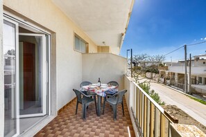 Een balkon met een tafel en stoelen, een schuifdeur en uitzicht op de straat.