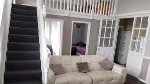 Ein Wohnzimmer mit einem beigefarbenen Sofa, einem weißen Tisch, einer Treppe und einem Schrank mit weißen Türen.