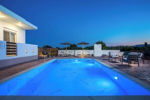 A swimming pool with lounge chairs and umbrellas, surrounded by a modern building.