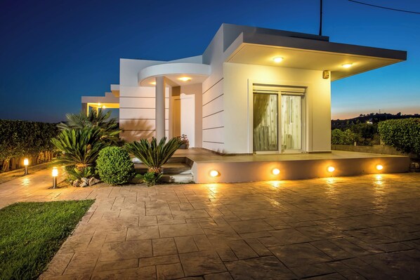 A modern house with a curved facade, a well-lit entrance, and a paved driveway.