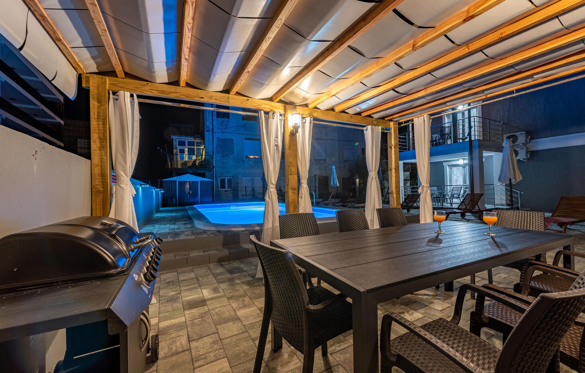 An outdoor patio area with a pool, wooden ceiling beams, and a dining table with chairs.